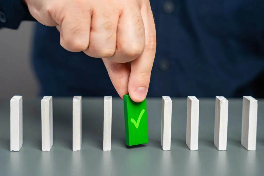 A hand stopping falling dominoes with a green piece.