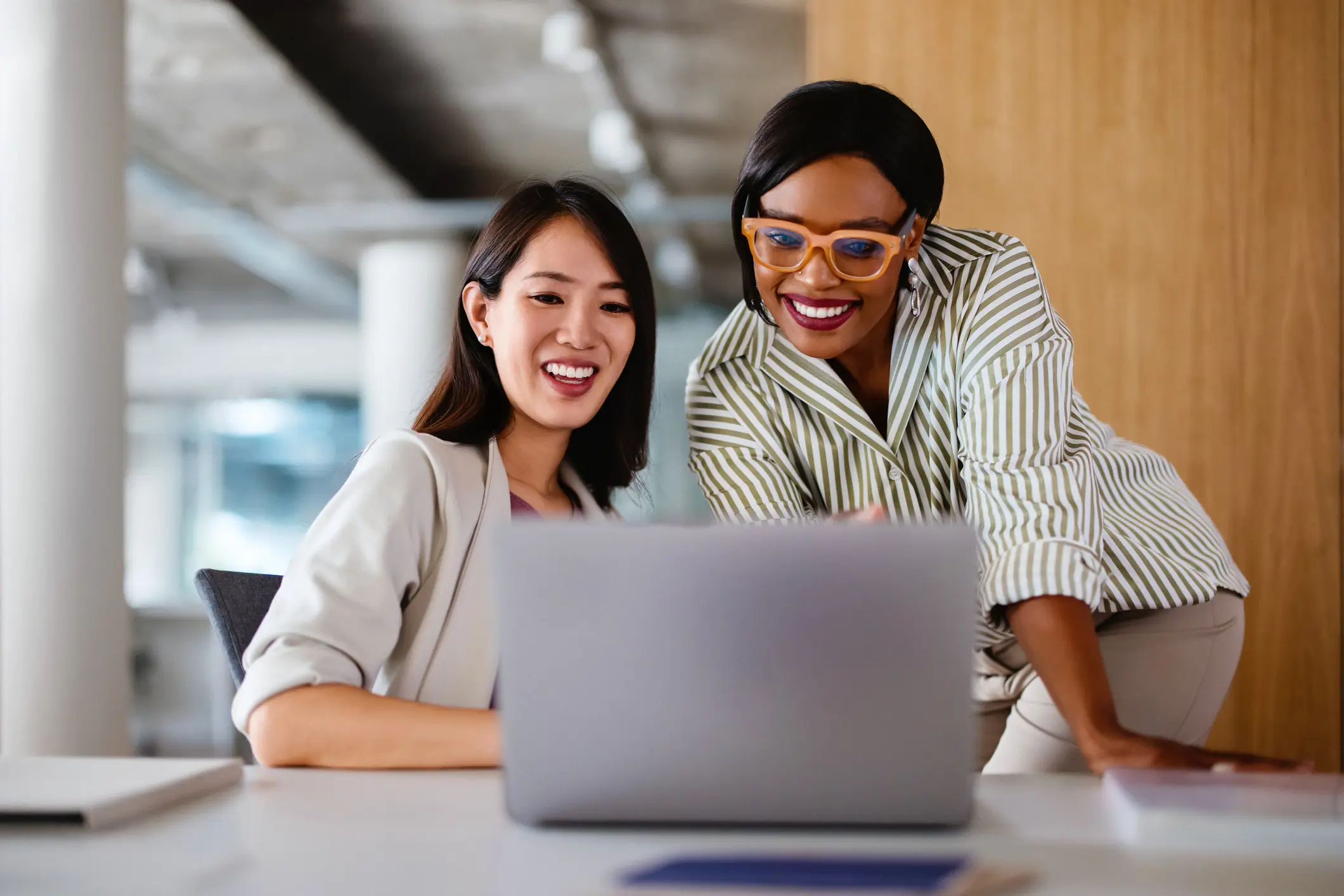 Two women smiling and looking at a laptop together.