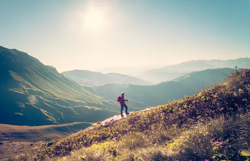 A person hiking on a sunlit mountain trail with scenic views.