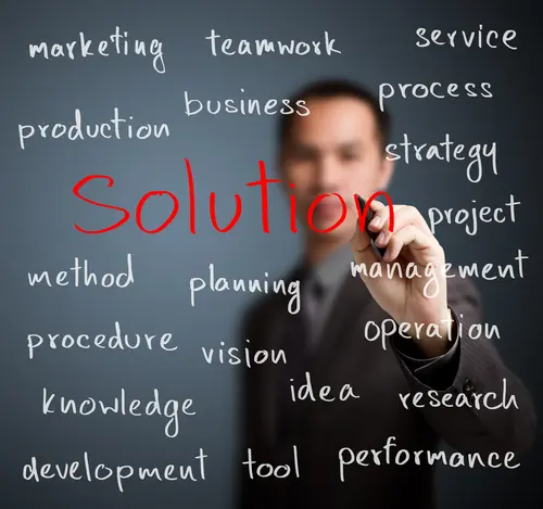 Blurred businessman pointing at the word 'Solutions' on a transparent board filled with business terms.