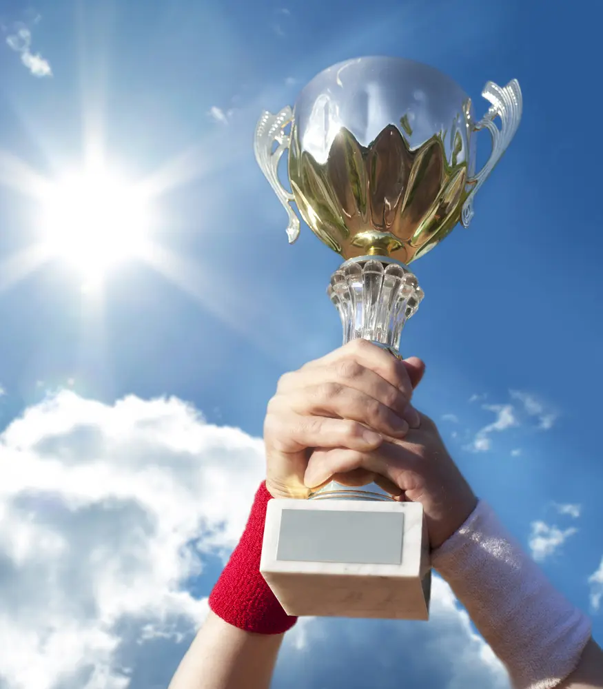 Hand holding a trophy up against a bright blue sky and sun.