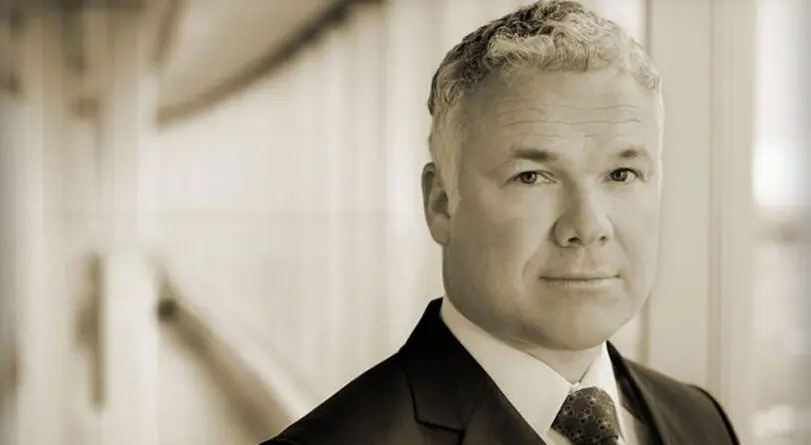 Portrait of a middle-aged man in a suit with a blurred background.