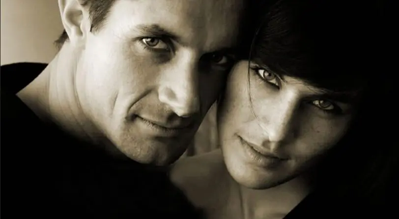 Close-up of a man and woman with intense expressions, in warm sepia tones.