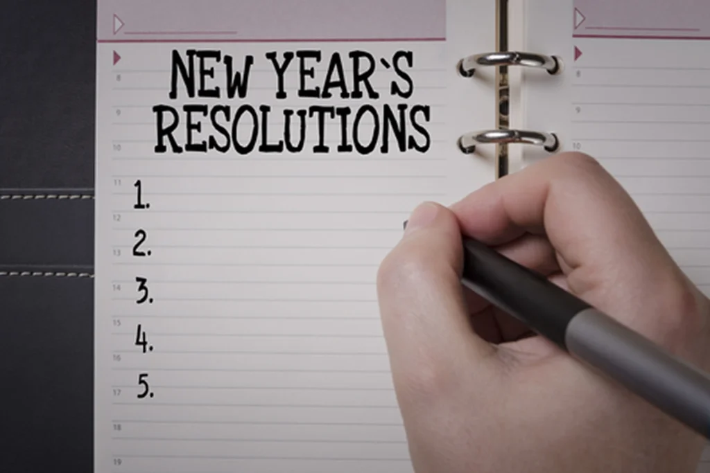 Hand writing New Year's resolutions on a lined notebook.